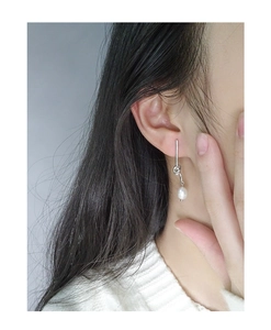Detail of S925 silver knotted earring with a white pearl on a model in white sweater