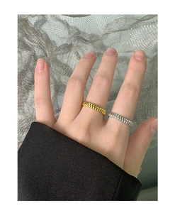 Detailed view of two minimalist gear-pattern rings in gold and silver on a finger