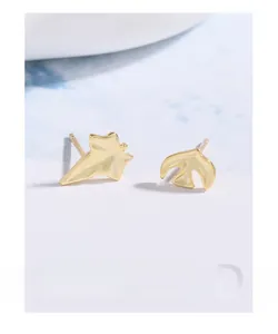 Macro detail of asymmetric S925 silver gold-plated leaf and flying bird stud earrings