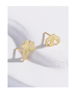 Detailed macro shot of matte gold asymmetric leaf and bird stud earrings on white stone