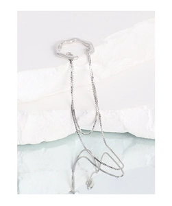 Macro detail of S925 sterling silver tassel ear cuff on a minimalist white stone background