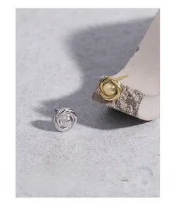 Detail of spiral hoop earrings in gold and silver finish on modern textured background