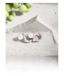 Détail macro de boucles d'oreilles en argent S925 et perles sur un socle en pierre