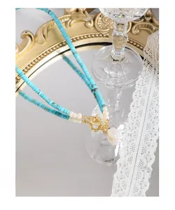 Dettaglio macro della collana bohémien in turchese con perla barocca su uno specchio