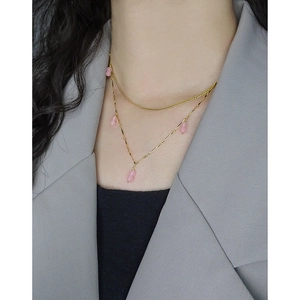 Double-layered gold necklace featuring pink agate beads worn by a model in a grey suit