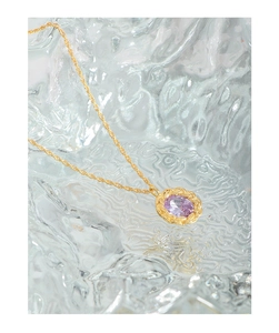 Macro detail of purple oval gemstone pendant with gold twisted wire border on necklace