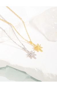 Detail of minimalist starburst necklaces in gold and silver on white stone