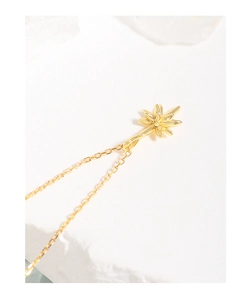 Macro view of a gold star pendant necklace resting on a minimalist white stone pedestal