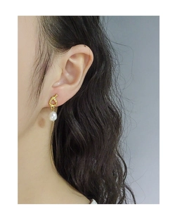 Close-up of elegant gold knot stud earrings with a white baroque pearl on ear