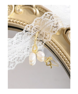 Close-up of gold liquid lava drop earrings with baroque pearls on white lace fabric