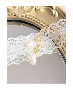 Detail of baroque pearl earrings with irregular gold metal texture on a vintage mirror