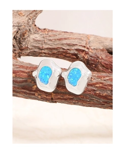 Macro shot of irregular silver earrings with blue opal stones on a wooden branch