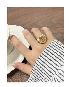 Gros plan d'une bague coeur dorée avec pierre rose et perles blanches au doigt