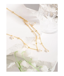 Detail of elegant gold Y-shaped pearl necklace on a white stone base with flowers