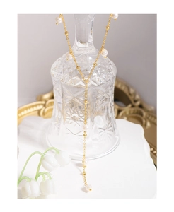 Detail of elegant gold Y-shaped pearl necklace draped over glassware with lily of the valley