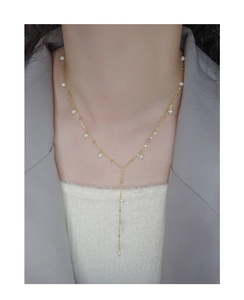 Detail of elegant gold Y-shaped pearl necklace worn on model with grey blazer