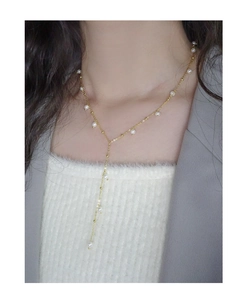 Detail of elegant gold Y-shaped necklace with white pearls worn on a female model