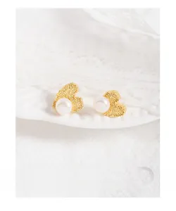 Detail view of heart-shaped gold earrings with textured surface and white pearl drop
