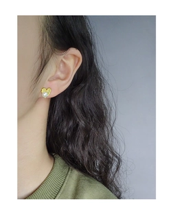 Detail of heart stud earring with textured gold surface and white pearl on ear