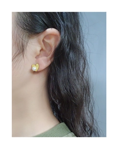 Close-up of model wearing textured gold heart earrings with white pearl inlay