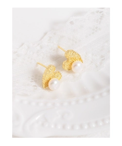 Macro detail of gold heart earrings with matte texture and dangling white pearls