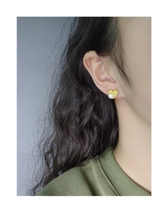 Close-up of heart-shaped gold stud earring with wrinkled texture and white pearl on model