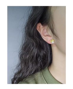 Close-up of a heart-shaped gold earring with a white pearl on a model's ear