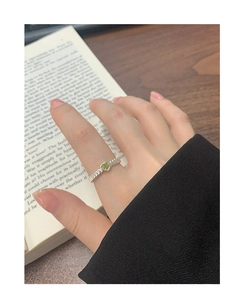 Close-up of S925 silver heart ring with green zircon and textured band on book