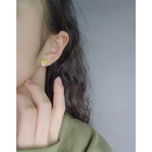 Elegant heart-shaped gold matte earring with a white pearl on a model's ear