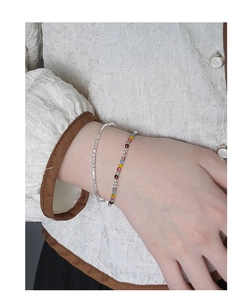 Detail of layered S925 silver fine chain and colorful bead bracelet on a female wrist