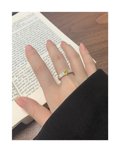 Detail of S925 silver ring featuring a heart-shaped yellow gemstone on a hand over a book