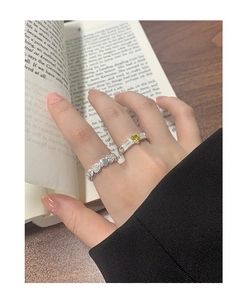Detailed view of silver heart-shaped band and yellow square gemstone ring set worn on hand
