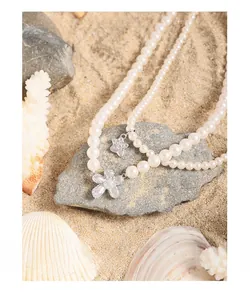 Detail of double-layer pearl necklace with zircon flower and star pendant on sandy beach
