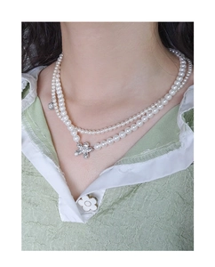 Close-up of double-layer pearl necklace with a sparkling silver floral pendant on model