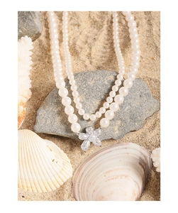 Macro detail of double-layer pearl necklace with elegant silver flower pendant on shell beach