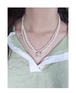 Detailed view of double-layer pearl necklace with silver flower and star pendant on a model