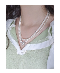 Close-up of double-layer pearl necklace with a silver butterfly pendant on a model
