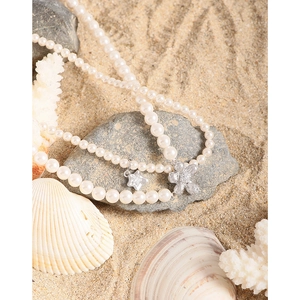 Double-layer pearl necklace with silver star and floral pendants on a beach reef background