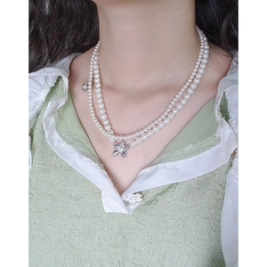 Double-layered pearl necklace with silver flower pendant on model in green shirt