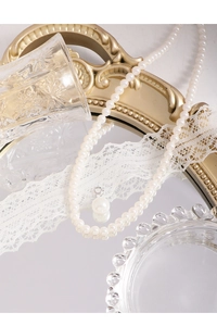 Elegant white pearl necklace detail with a large round pendant on a vintage mirror surface