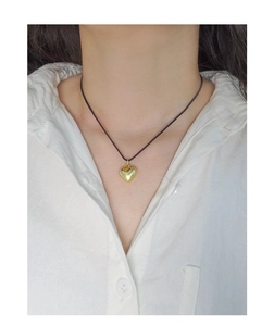 Gros plan détaillé du pendentif coeur 3D doré sur un collier en cordon noir minimaliste