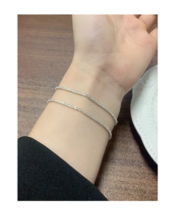 Macro shot of minimalist silver layered bracelets on wrist over a wooden background