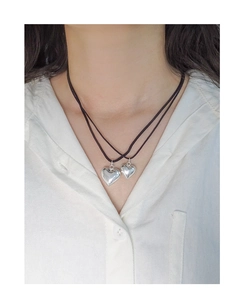 Gros plan de pendentifs double cœur sur un cordon noir porté sur une chemise blanche