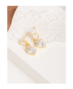 Détail de boucles d'oreilles cœur en zircon doré sur un fond de dentelle blanche délicate