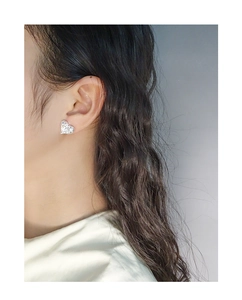 Close-up of heart-shaped silver earrings with sparkling zircon on model ear