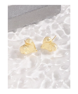 Detail of gold heart stud earrings with irregular lava texture on white water ripple base