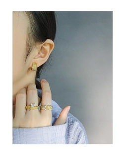Detail of twisted gold jewelry set featuring square zircon ring and braided hoop earrings