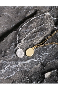 Detail of gold and silver irregular lava coin necklaces on textured natural stone