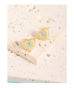 Détail macro de boucles d'oreilles cœur dorées avec zircon bleu et texture en métal côtelé