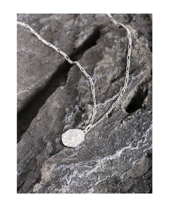 Macro detail of S925 sterling silver irregular coin pendant on a rocky texture background